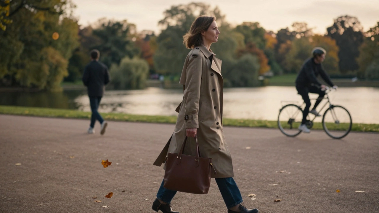 A woman in a trench coat walking through Hyde Park at dusk, autumn leaves, serene atmosphere.