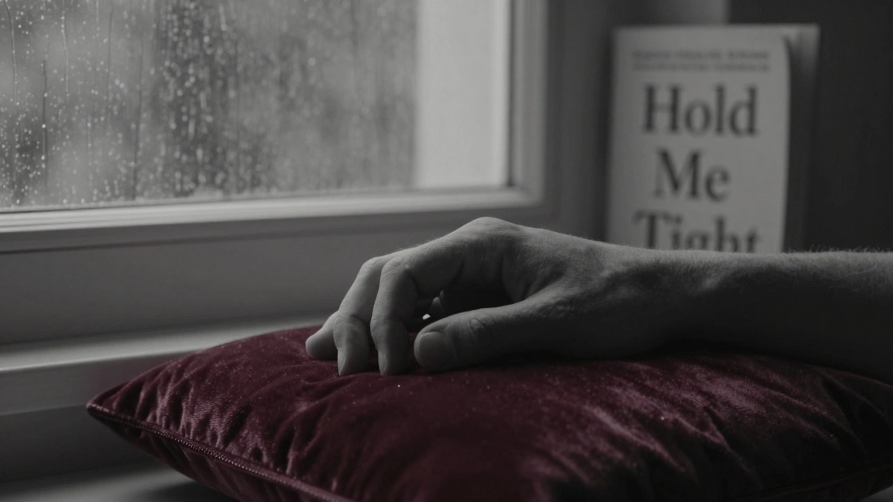 Two hands gently clasped on a velvet cushion, with a blurred window and book visible behind, conveying quiet emotional connection.